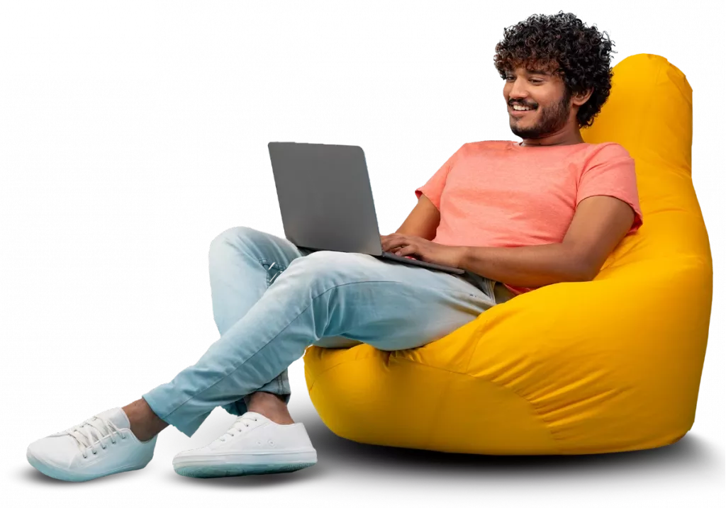 Homem sorridente sentado em uma poltrona de puff amarela, usando um laptop, representando o trabalho confortável e remoto utilizando o software Immobile da Alterdata.